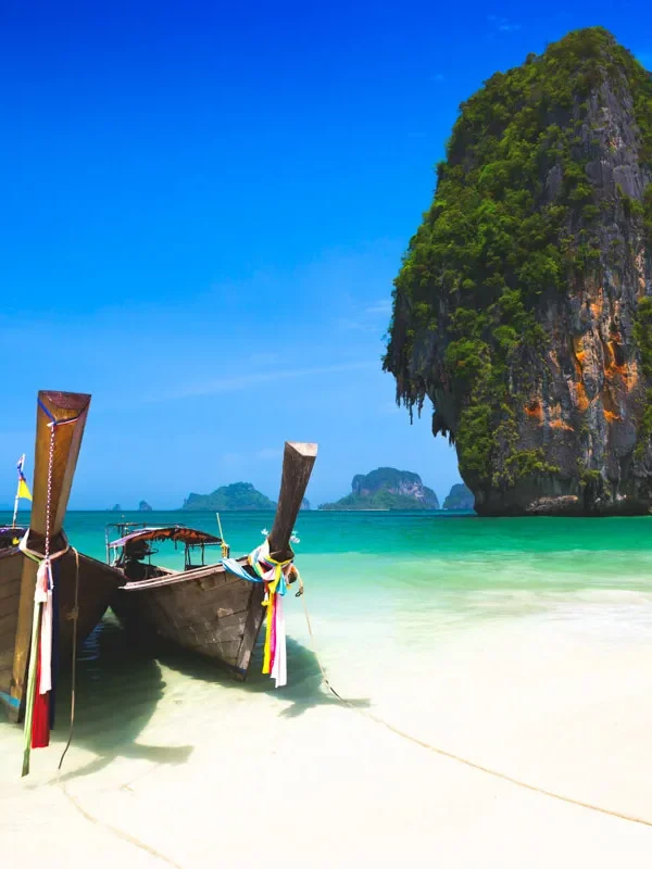 wo traditional long-tail boats on the sandy beach in Krabi with clear blue water