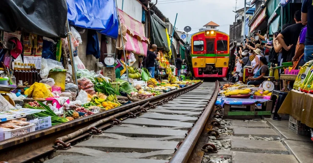 Train passing through the middle of Maeklong Railway Market with vendors pulling back their stalls