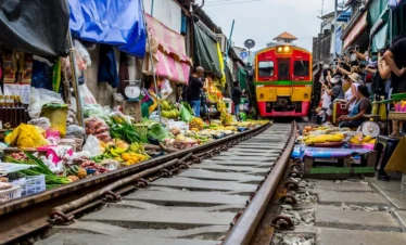 Train passing through the middle of Maeklong Railway Market with vendors pulling back their stalls