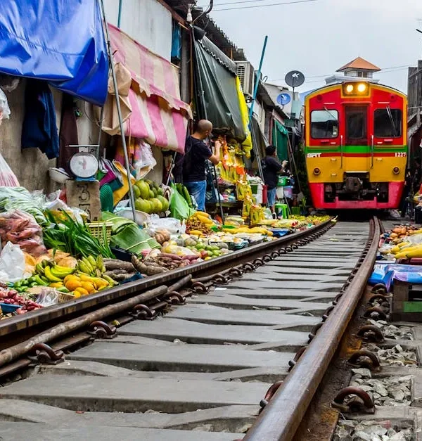 Train passing through the middle of Maeklong Railway Market with vendors pulling back their stalls