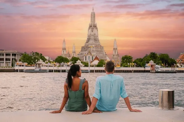 couple came from uk sitting near chaopraya river with watt arun view