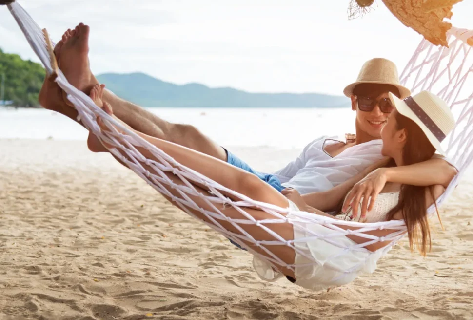 UK tourists enjoying a beach holiday in Thailand with traditional longtail boats at sunset